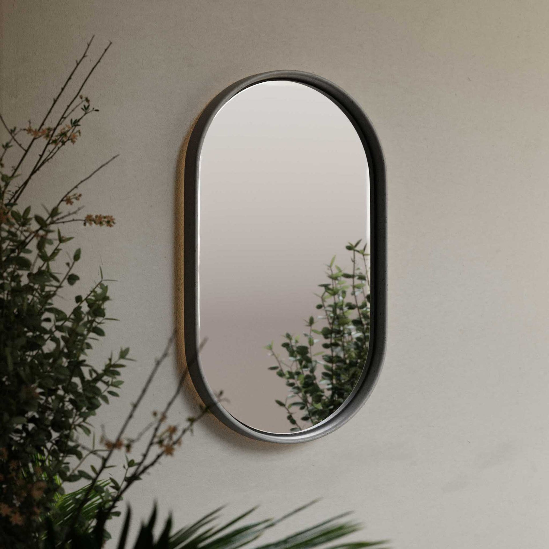 The Lunar Concrete Mirror, an elegant oval-shaped mirror with a smooth, curved concrete frame, mounted on a neutral-toned wall.