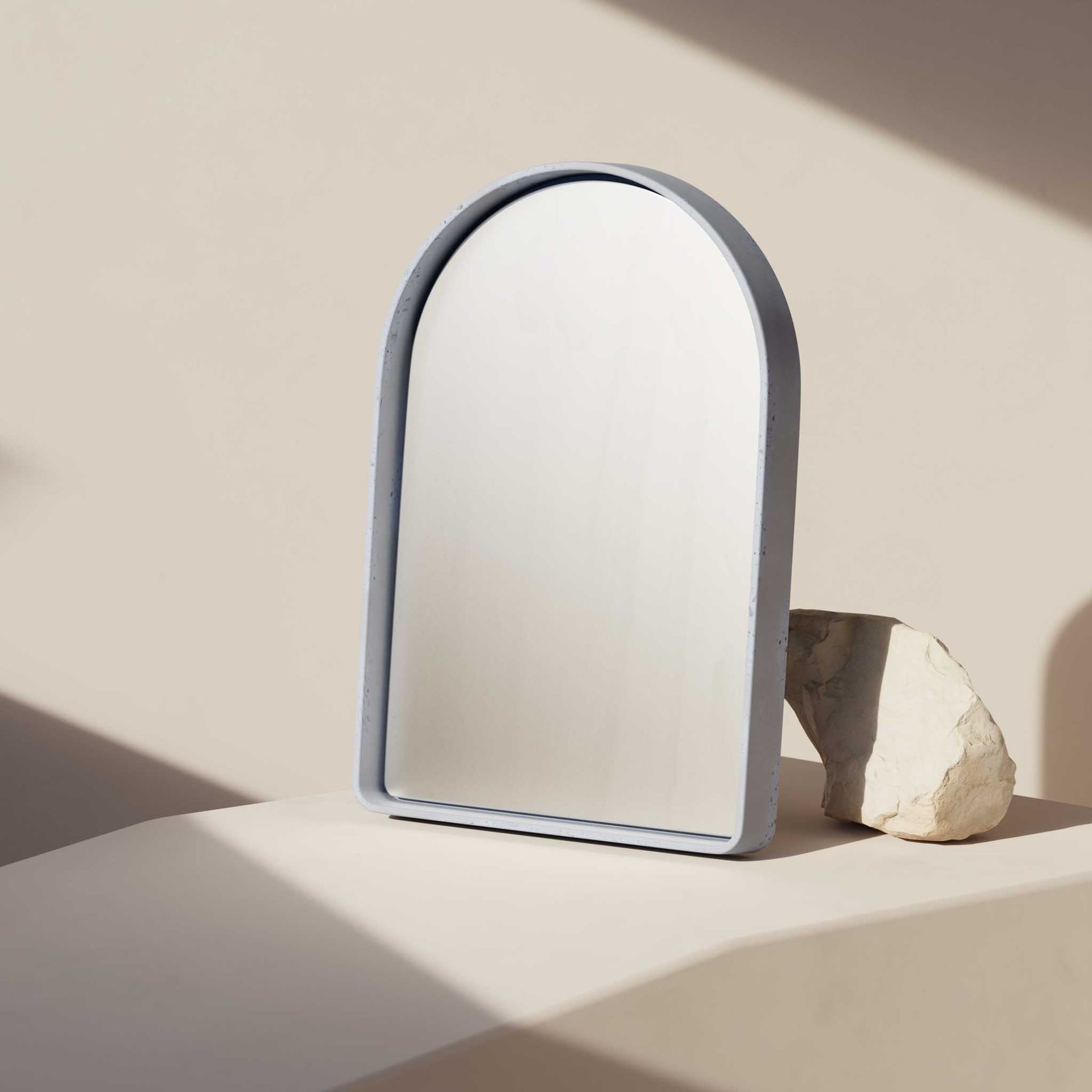 The Arc Concrete Mirror leaning on a rock in a sunlit room
