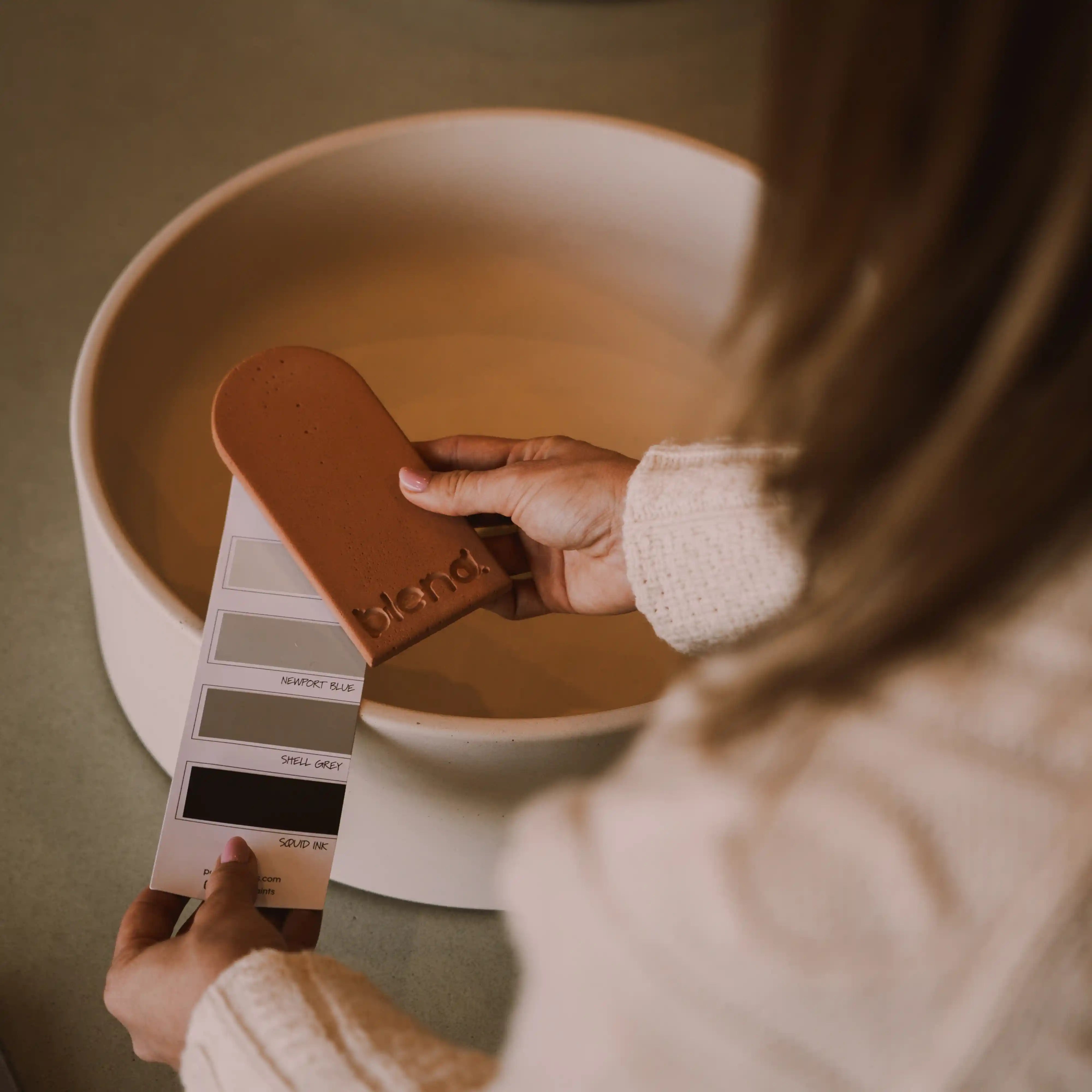 A woman holding a concrete colour sample in front of a concrete basin.
