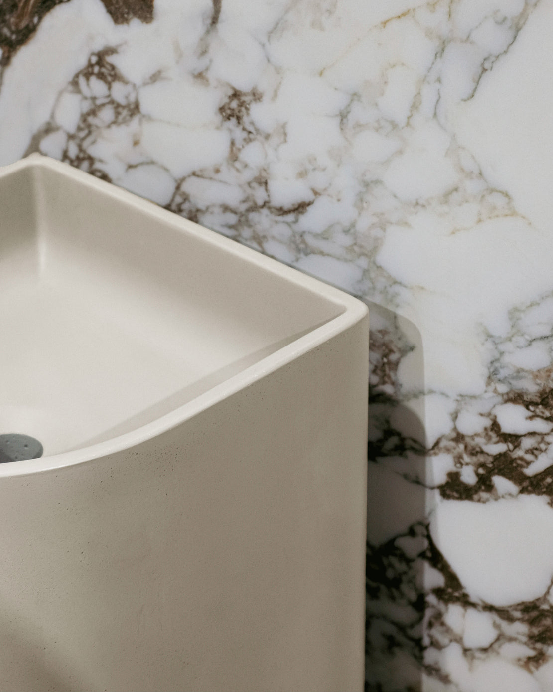 The Aurora Concrete Pedestal Basin against a porcelain tile in the Kaolin Surfaces showroom in Sydney.