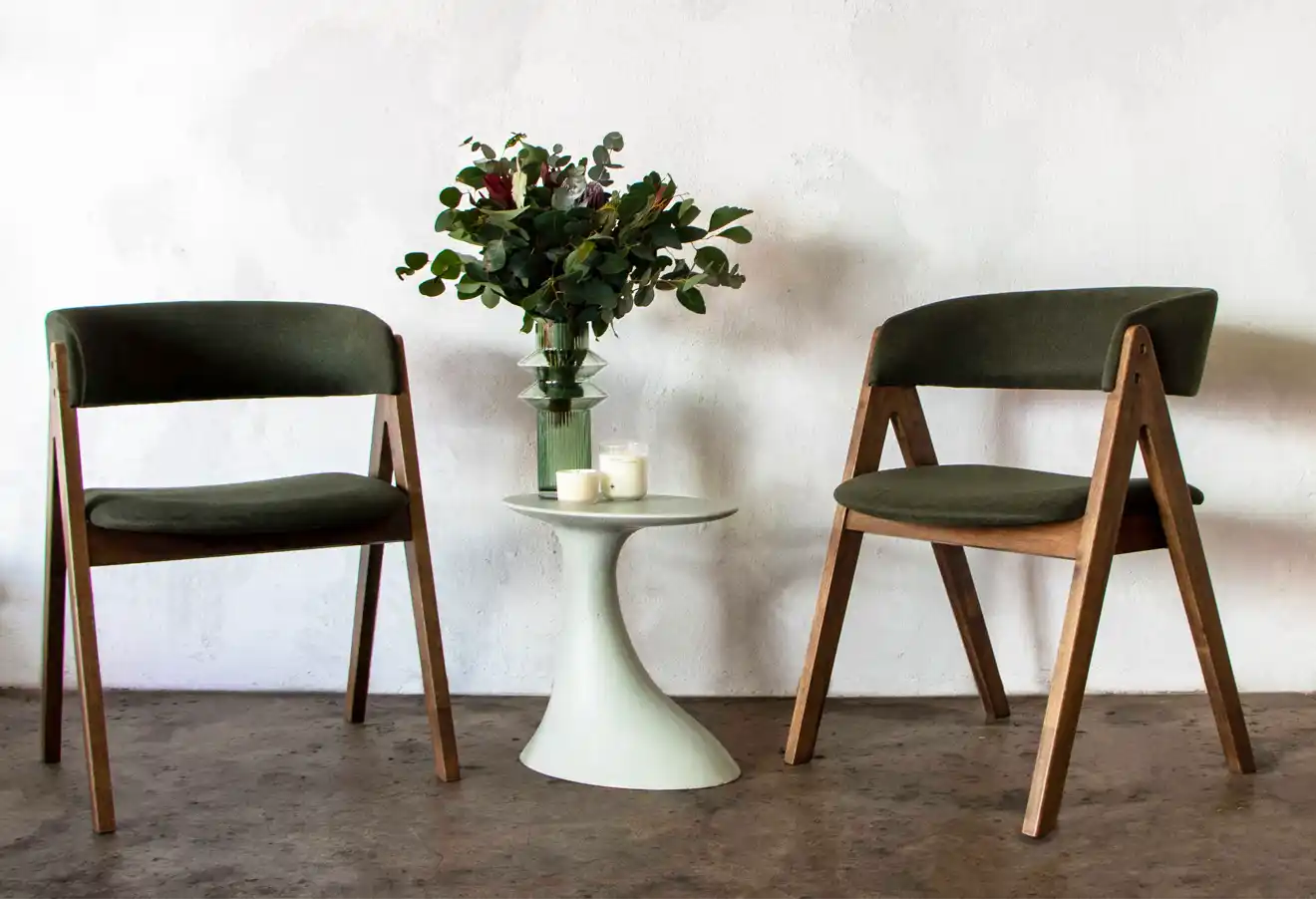 The Oasis Concrete Side Table in Rainforest Green between two to dark green and walnut dining chairs in a well light minimalist living room.