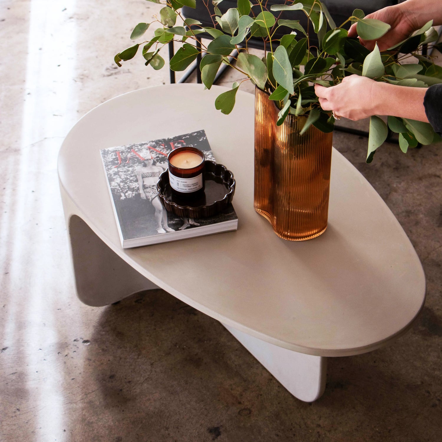 A top view of the curves of the Riviera Concrete Coffee Table with two hands adjusting flowers in a vase.