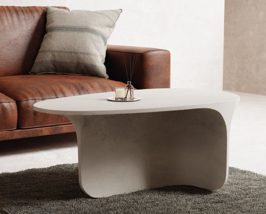 A whitehaven Riviera Concrete Coffee Table on a grey rug with a brown leather couch. 