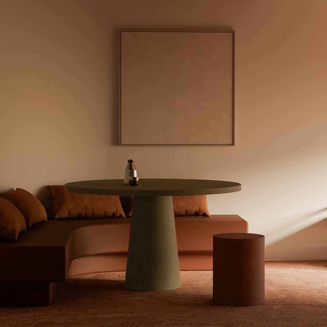 Olive-toned custom concrete dining table with a tapered base by Blend Concrete Design, set against a curved banquette with rust-coloured cushions in a warm, minimalist interior.