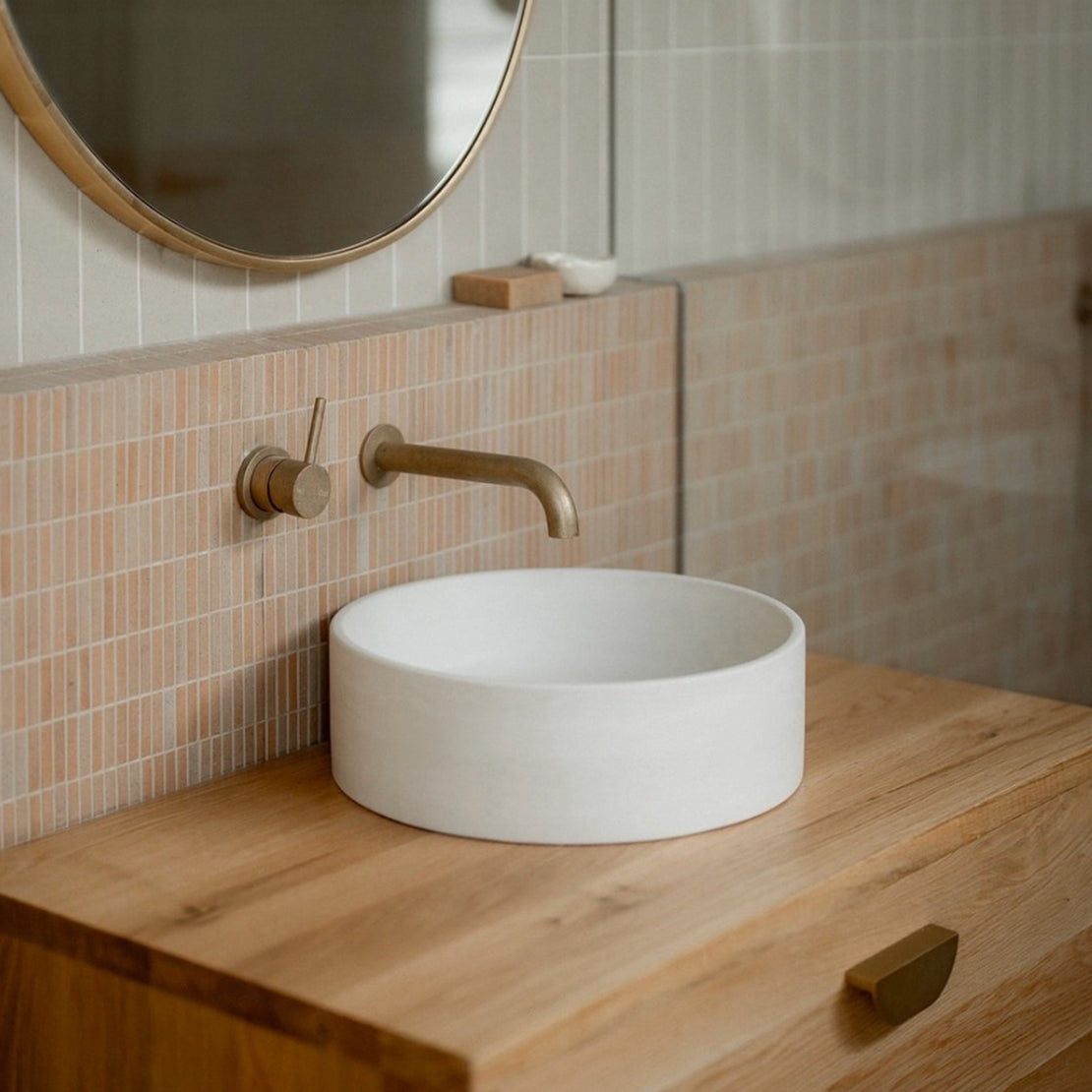 The Comet Concrete Basin in Whitehaven on a wooden vanity with brass tapware and peach tiling.