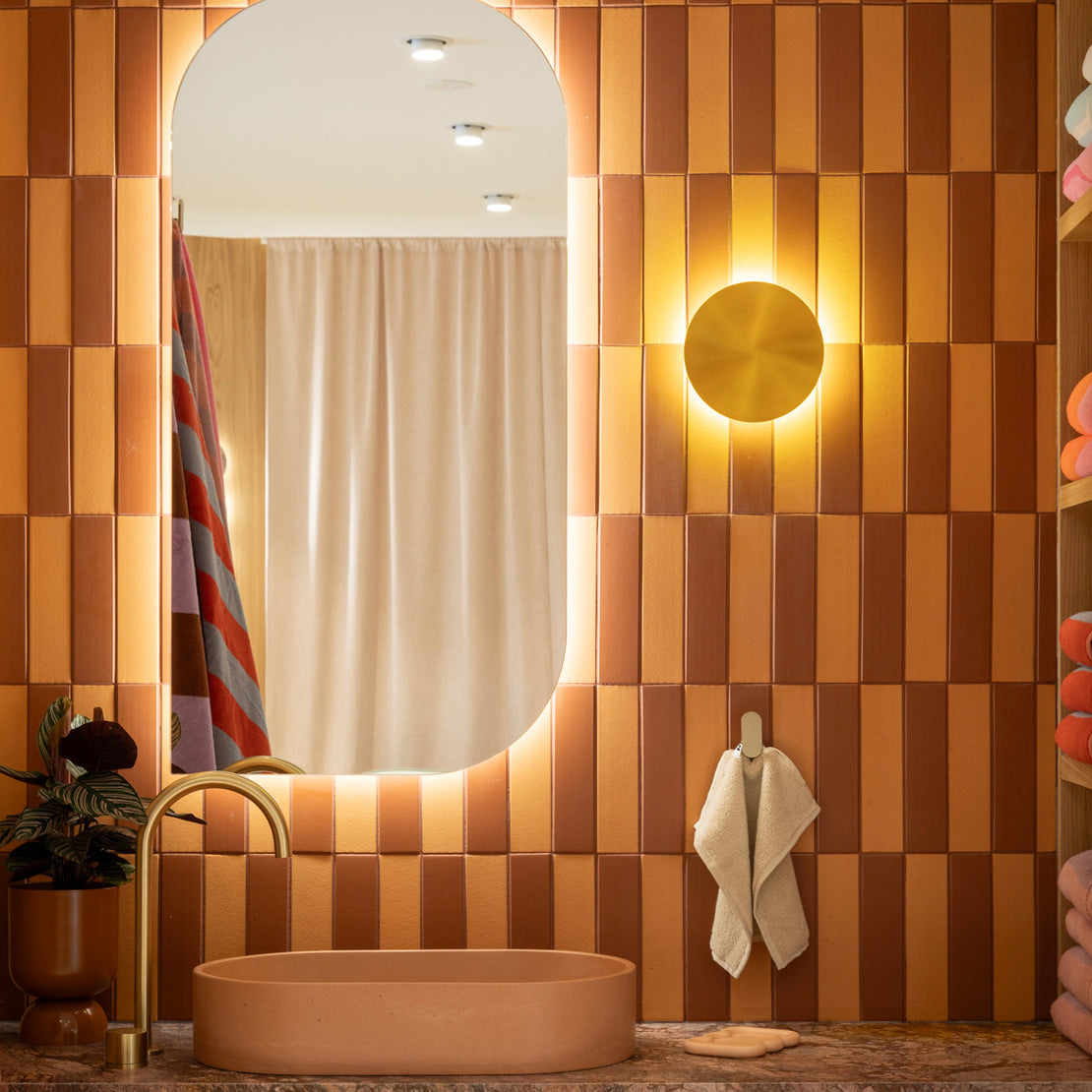 The Eclipse Concrete Basin in the colour Dingo. The bathroom features brown and orange subway tiles and gold tapware