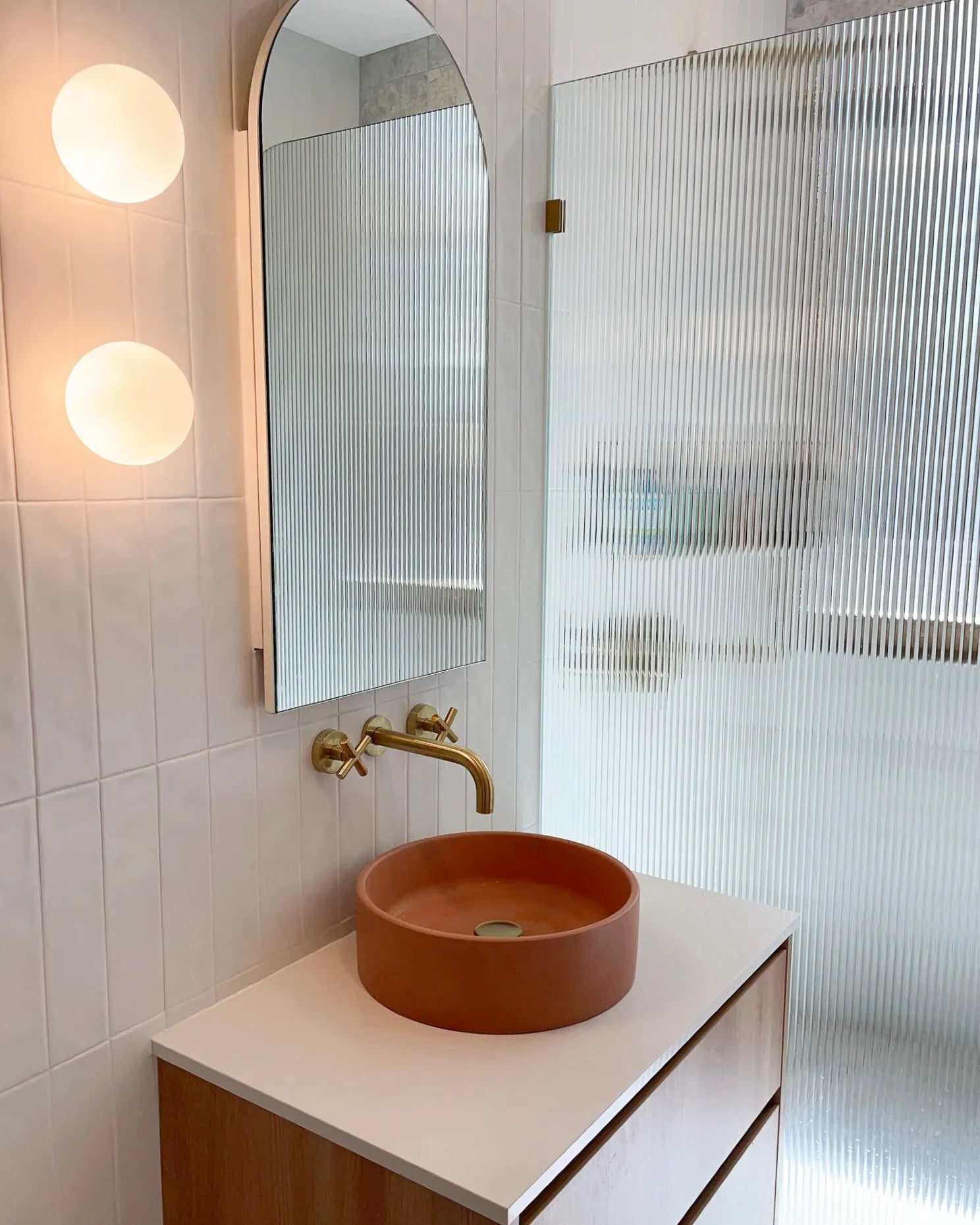 The Comet Concrete Basin in Dingo in a tiled bathroom with warm globe shaped lights and gold tapware