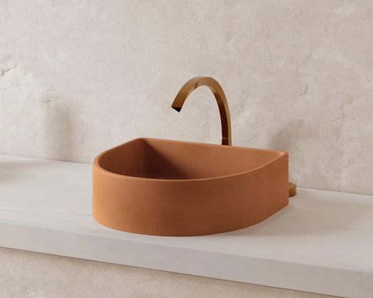 The Crescent Concrete Basin in a terracotta colour on a white concrete vanity top against a microcement rendered wall. 