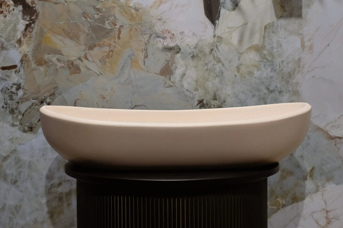 The Lyra Concrete Basin in a soft, neutral tone, featuring an elegantly curved, boat-like form with smooth, flowing edges.