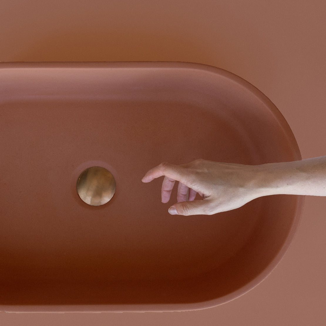 The Eclipse Concrete Basin with a clay coloured background and hand reach out.