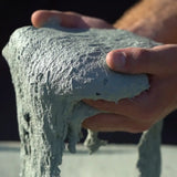 A close up of two hands holding green wet concrete.