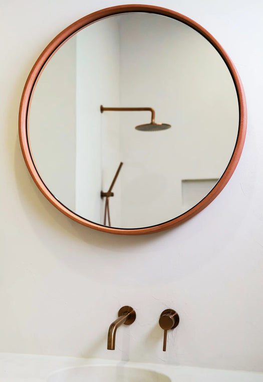 A Dingo (terracotta coloured) Sol Concrete Mirror installed on a rendered wall over a white concrete vanity top.