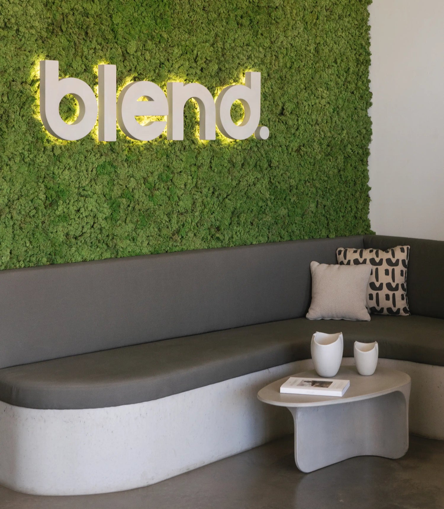 A concrete sign of the word 'blend' on a moss wall behind a concrete bench seat in the Blend Concrete Design showroom.