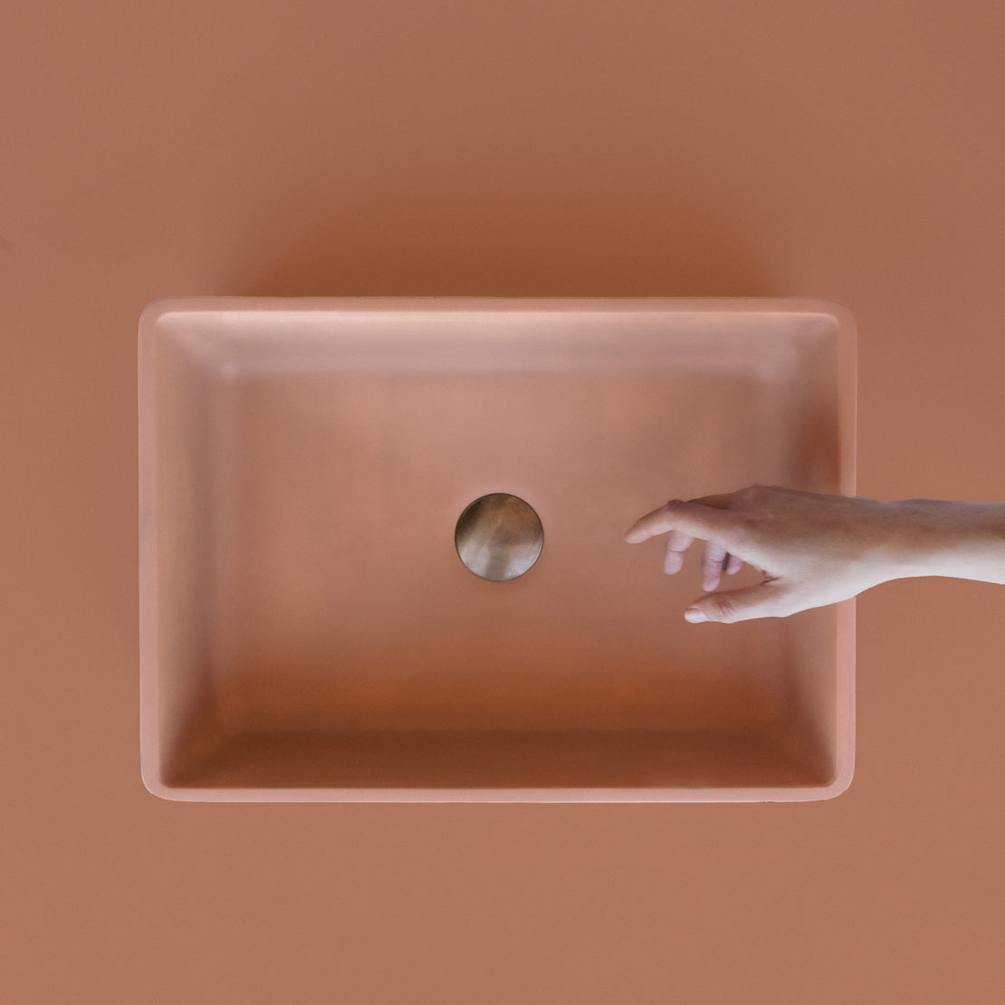 The Nova Concrete Basin with a clay coloured background and hand reach out.