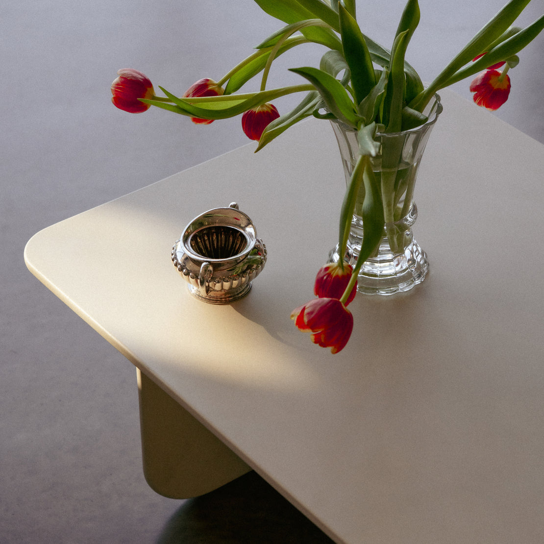 The Tor Concrete Coffee Table with a vase of red tulips sitting on top.