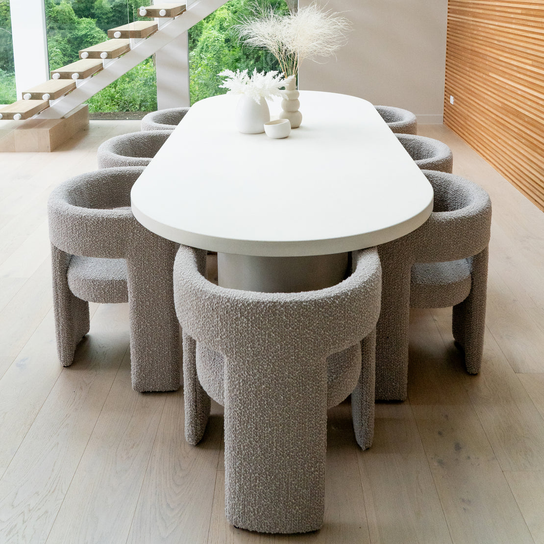 The Verona Concrete Dining Table in Whitehaven situated in a spacious dining space with grey material upholstered chairs.