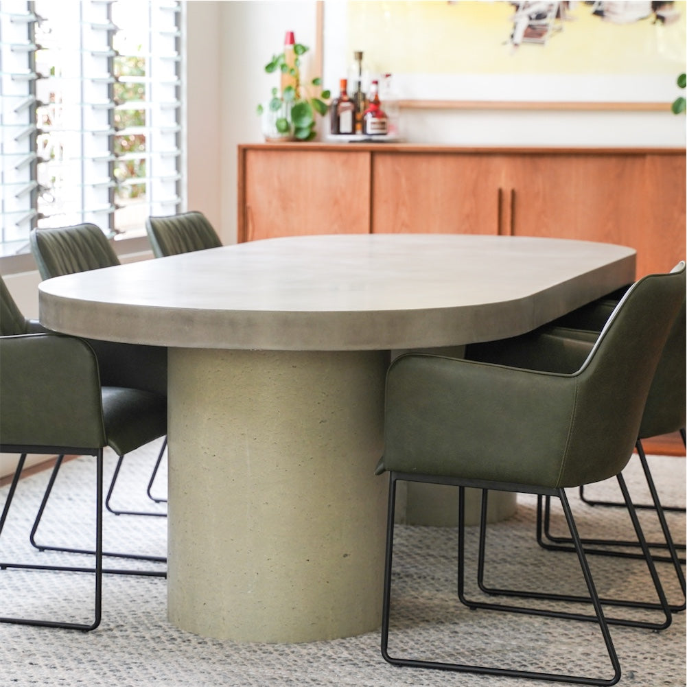 A Verona Concrete Dining Table with an arrangement of green leather chairs. 