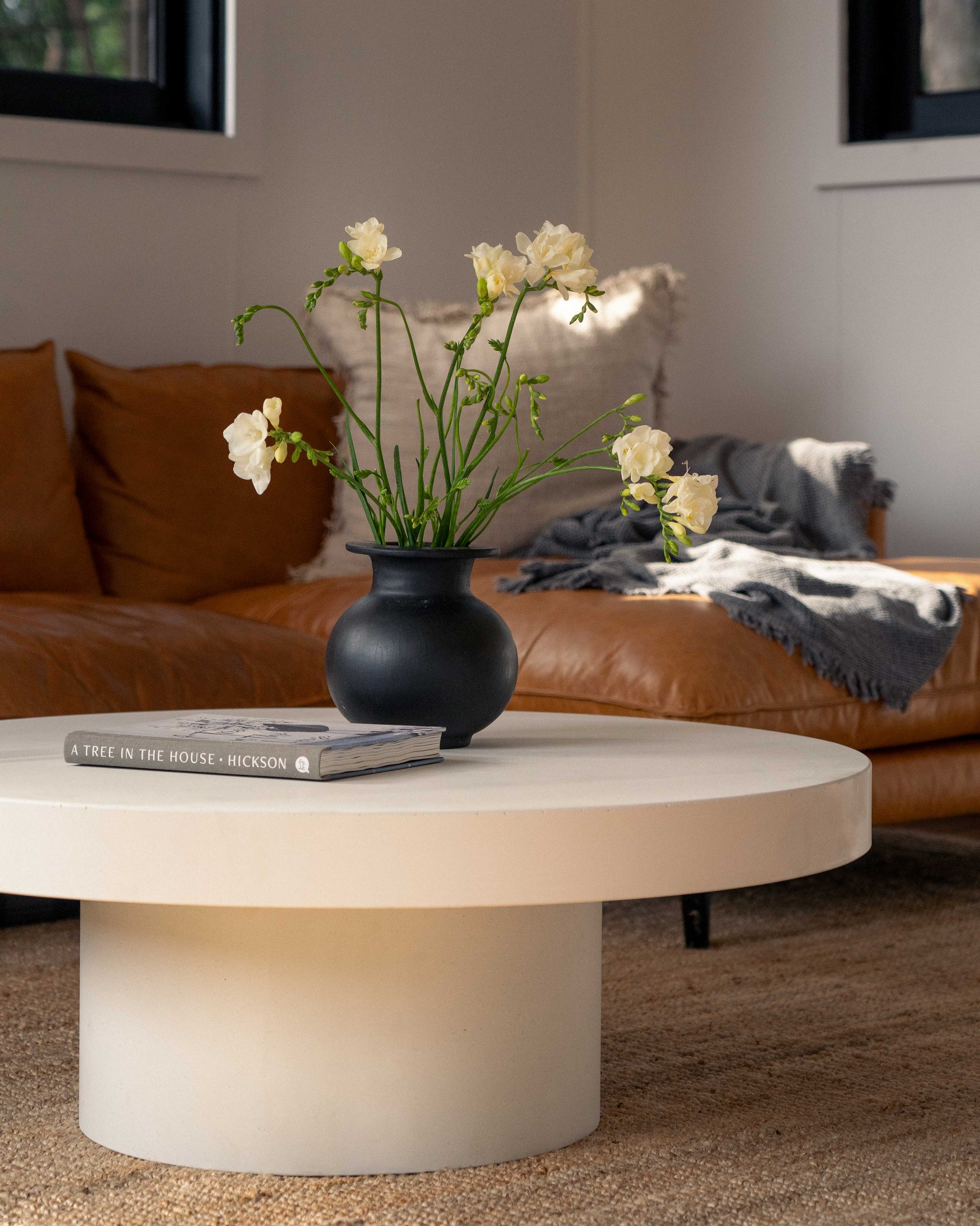 The Siena Concrete Coffee Table with a vase of white flowers sitting upon it.