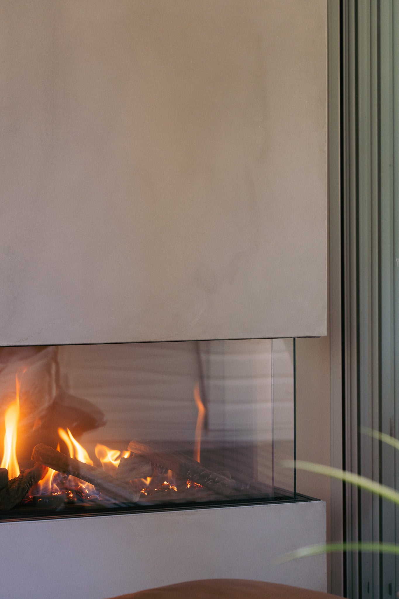 A custom concrete fireplace surround with a smooth, refined finish, framing a modern gas fireplace enclosed in glass, with warm flames flickering above realistic ceramic logs.




