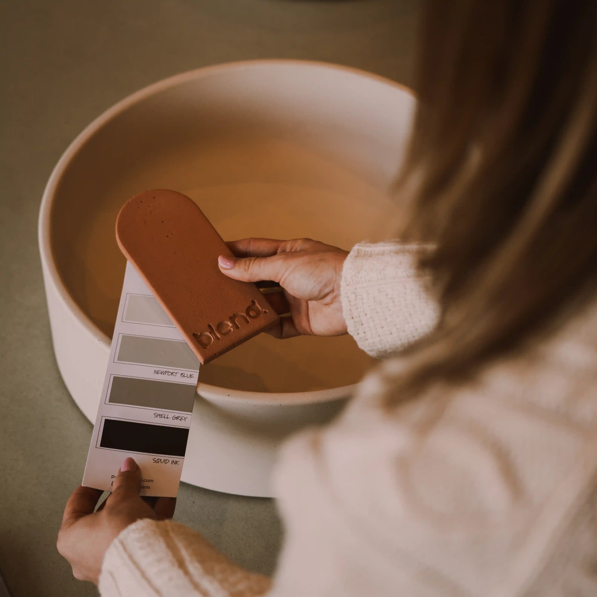 A woman holding a concrete colour sample in front of a concrete basin. 