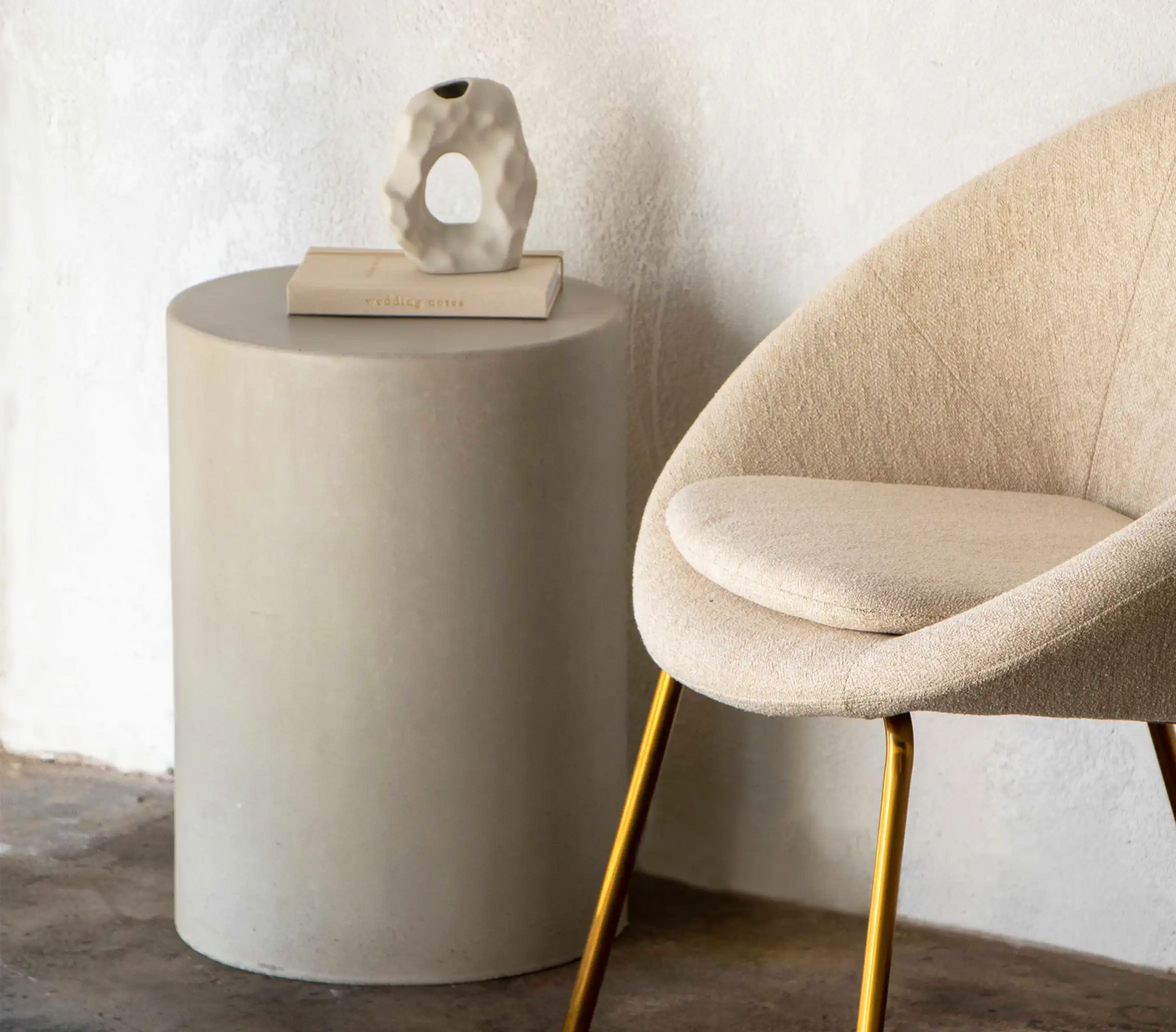 A Mist Grey Dune Concrete Side Table next to a round modern cream occasion chair with brass legs.