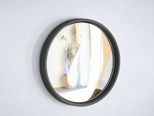 A small Storm Grey Sol Concrete Mirror with the reflection of a light living room. 