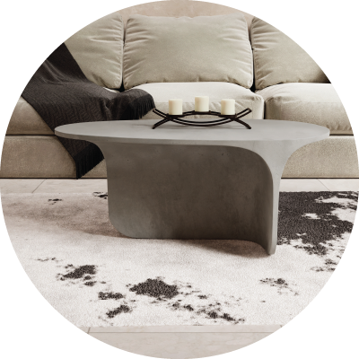 A side view of the Stingray Grey curved Riviera Concrete Coffee Table on a cow skin rug in front of a light grey couch. 