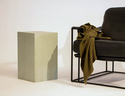A Rainforest Green coloured Sahara Concrete Side Table next to a black leather Coco Republic occasional chair.
