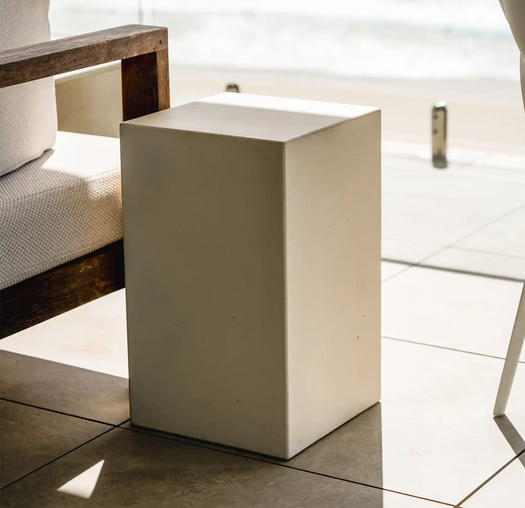 A Whitehaven Sahara Concrete Side Table on the veranda of a coastal beach apartment complementing a timber and white couch. 