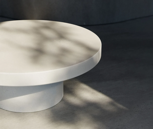A white round concrete coffee table on a concrete floor.