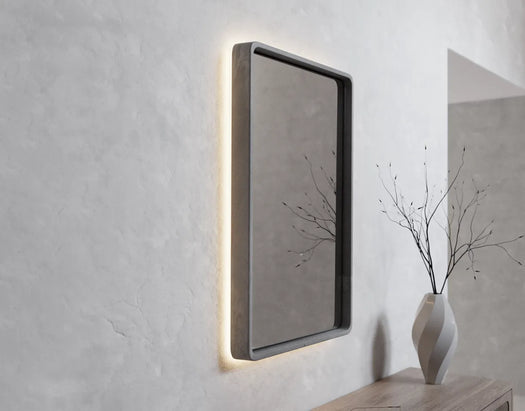 A Stellar Concrete LED mirror on a white micro cement rendered wall in a bright bedroom with a timber console unit.
