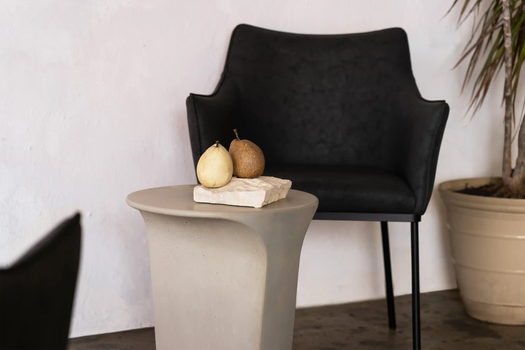 A Bilby Grey Alpine Concrete Side Table surrounded by simple decor and a dark seat.