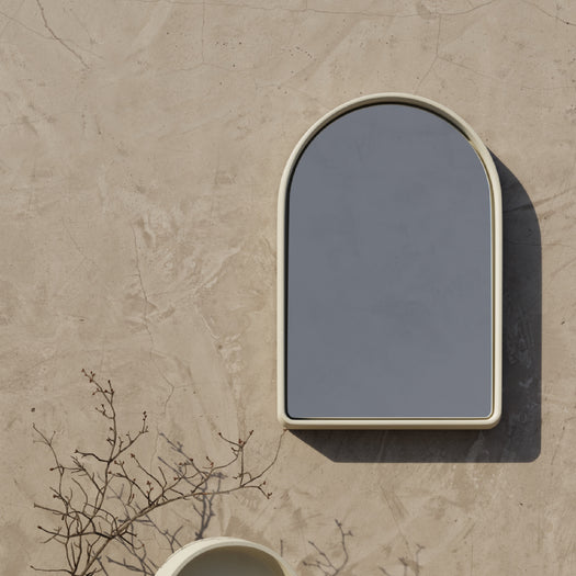 A sand Arc Concrete Mirror on a textured wall. 