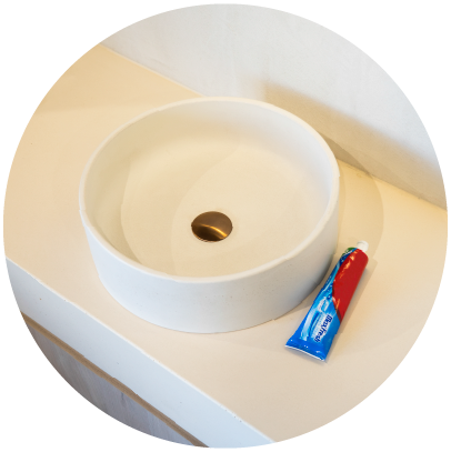 A round Comet Concrete Basin in the colour whitehaven on a white concrete vanity top next to a tube of toothpaste.