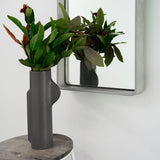 A small Koala Grey Stellar Concrete Mirror on a white wall with a grey vase in front. 