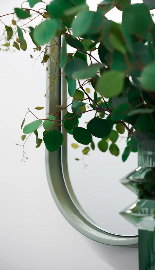 A close up of the Lunar Concrete Mirror in the colour Rainforest Green with a vase and eucalyptus in the foreground.