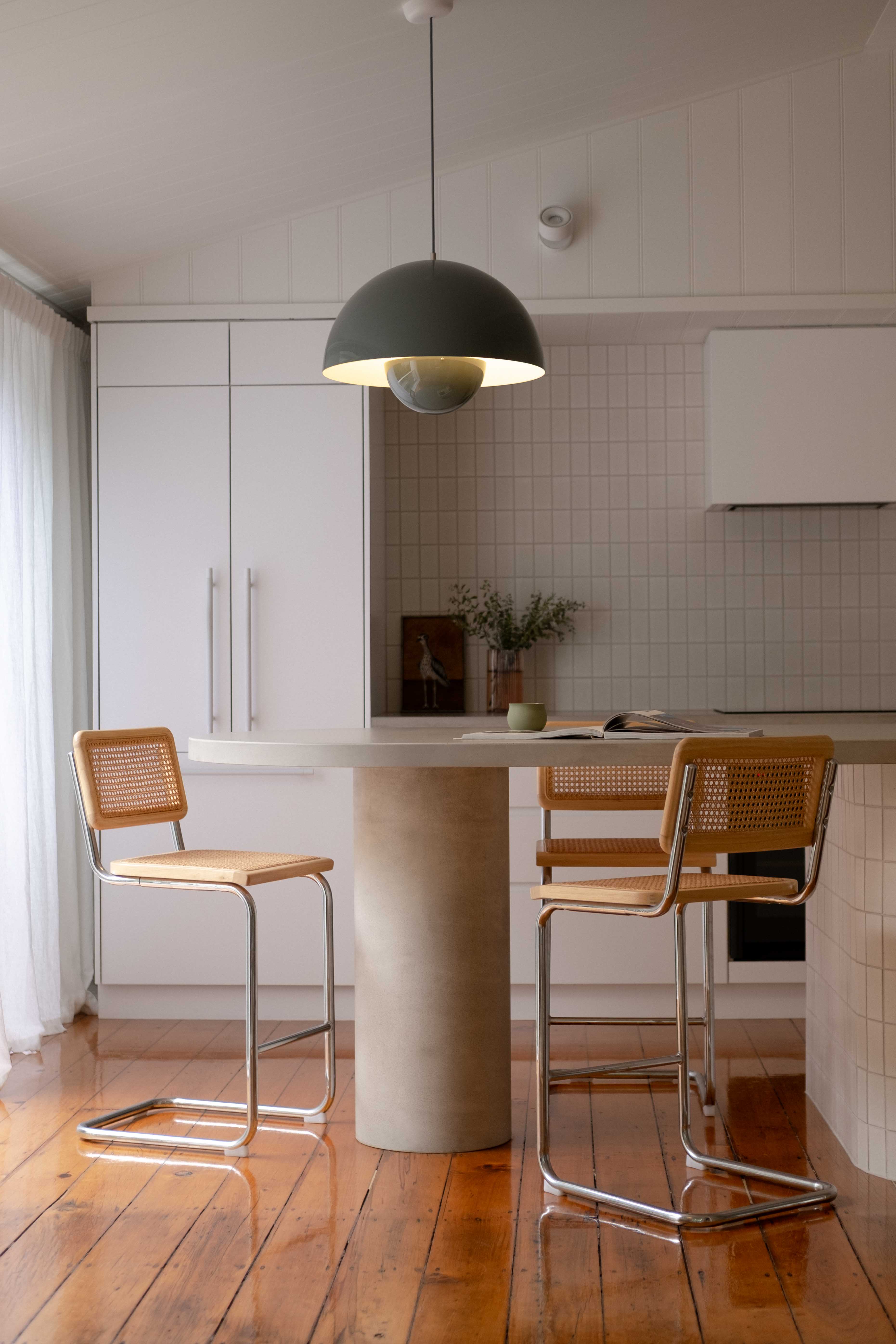 Custom concrete island kitchen bench with a rounded pillar base by Blend Concrete Design, styled with woven cane bar stools and soft neutral finishes in a light-filled, modern kitchen.