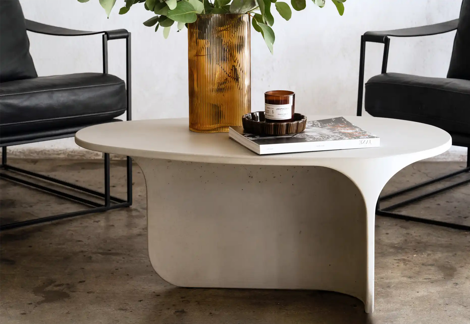A Mist Grey Riviera Concrete Coffee Table set with two black leather Coco Republic occasion chairs with a vase and magazine.